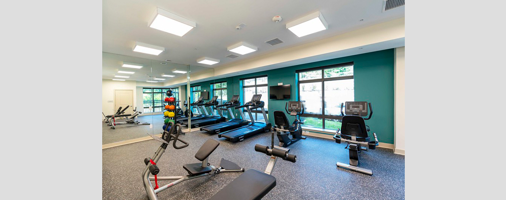 A modern fitness center with several treadmills, recumbent exercise bikes, free weights, and exercise benches.