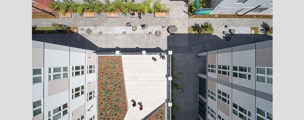 Aerial photograph of a raised courtyard framed by two buildings and a landscaped walkway below.