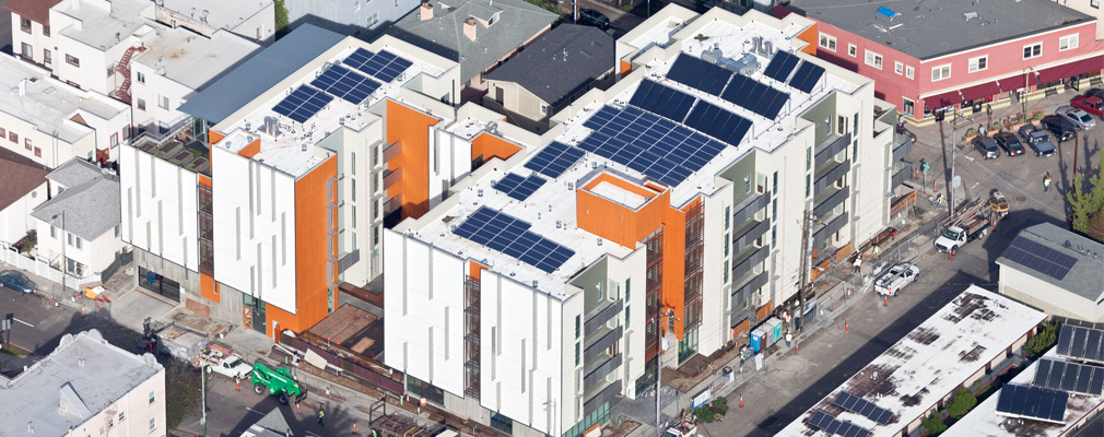 A top view of a nearly-complete five-story apartment building, topped with banks of solar panels.