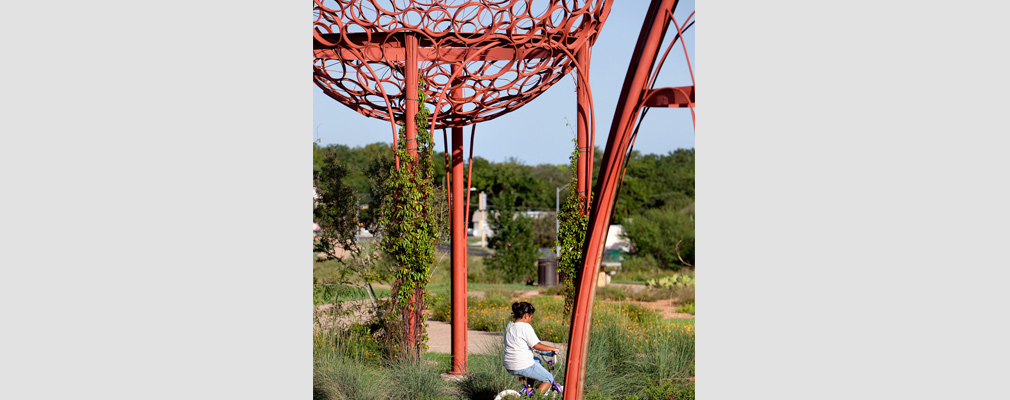Photograph of a Mueller resident bicycling in a park with native plants and public art.