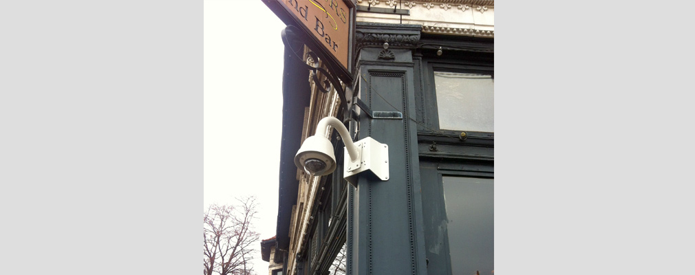 Photograph of a security camera affixed to the corner of a commercial building.