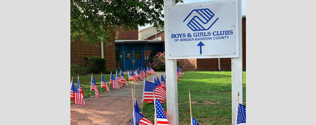 Photograph of a sidewalk leading to a doorway lined with American flags and marked with a sign containing the logo of the Boys & Girls Clubs of Winder-Barrow County.