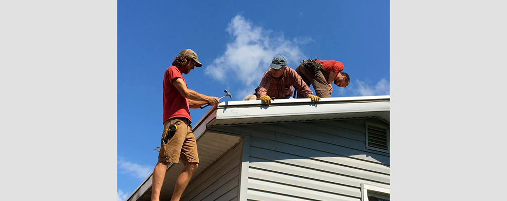 Photograph of three men working on the roof of a house.