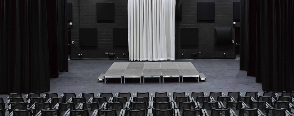 Photograph of the interior of a black box theater, with audience seating in front of an adjustable stage.