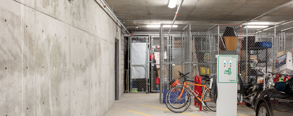 Photograph inside a concrete garage, with a charging station in front of a bicycle stand and wire storage units.