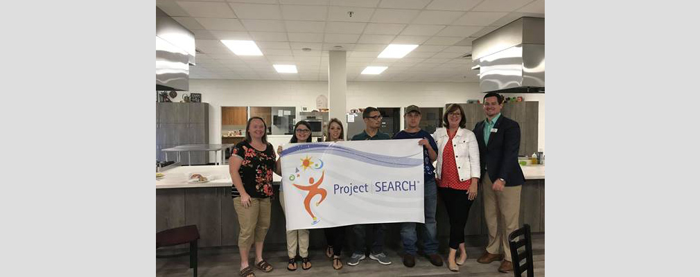 Photograph of seven people holding up a banner that reads “Project SEARCH.”