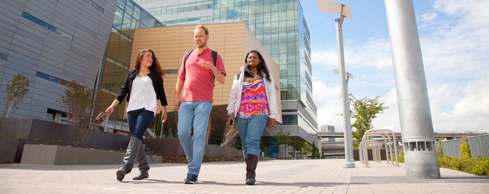 Photograph of three students walking in front of a multistory academic building.