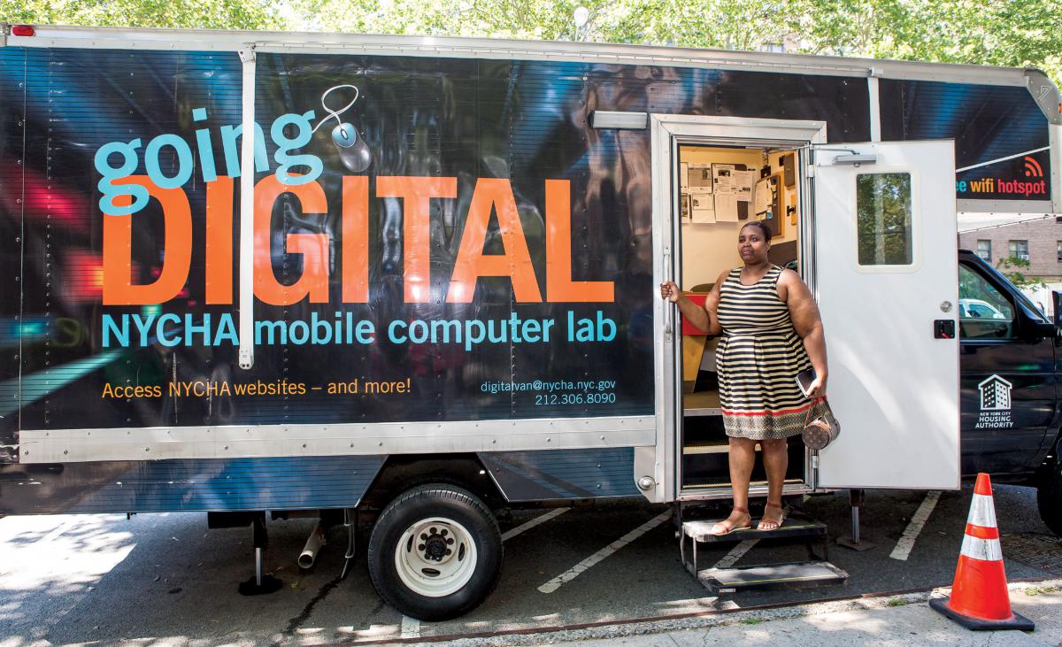 A woman stands on the steps of an RV that functions as a mobile computer lab.
