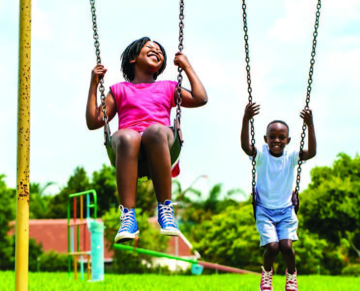 A boy and girl smile on swings in a park.