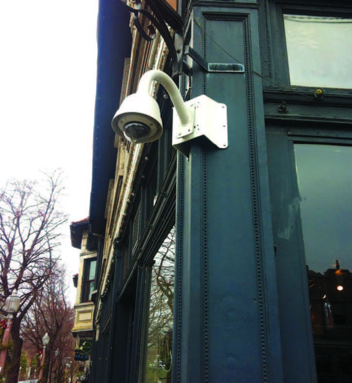 A close-up of a surveillance camera mounted on the corner of a building.