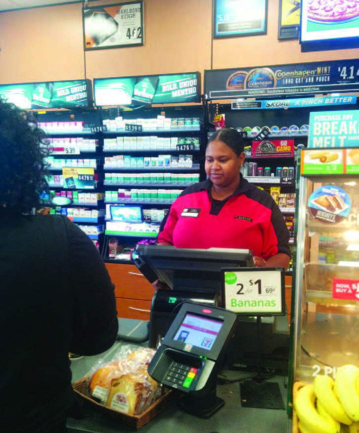 A young woman behind the checkout counter of a 7-11 attends to a customer.