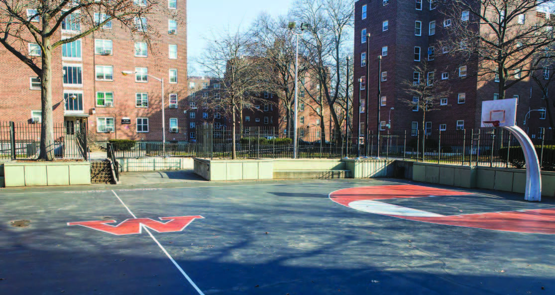 A basketball court in front of red brick apartment buildings.