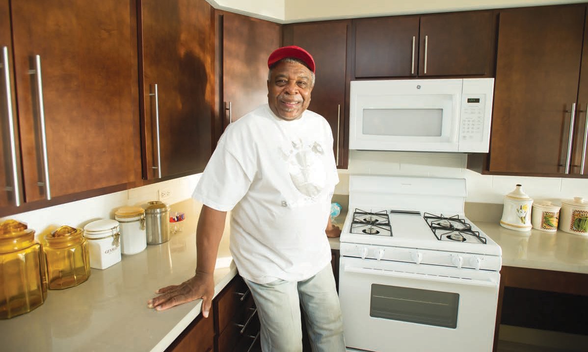 Man standing with his back against the counter in a kitchen with a range stove and microwave.