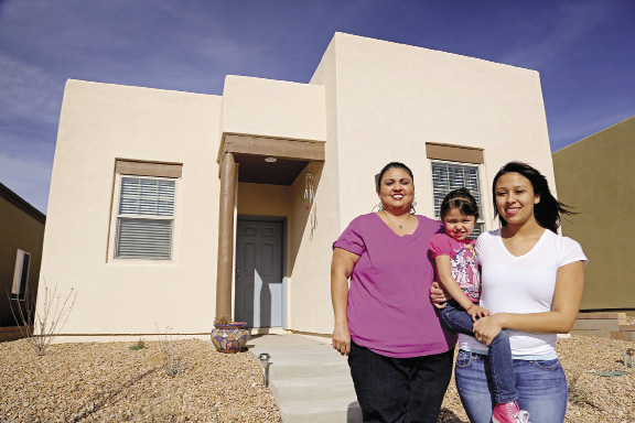 A mother and her two daughters stand in front of their new home.