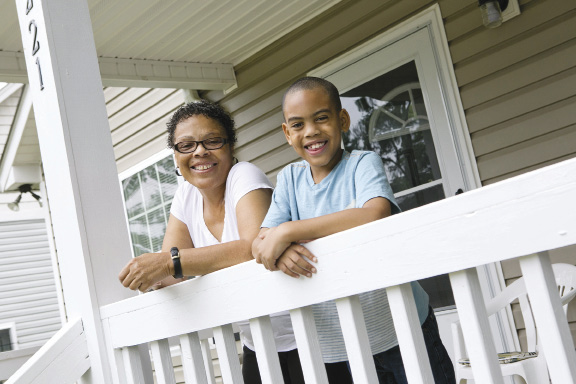 A woman and her grandson stand leaning on the railing of her home’s front porch.