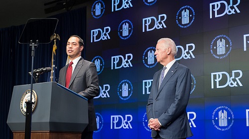 Photograph of HUD Secretary Julián Castro speaking at a podium onstage, with Vice President Joe Biden standing to his left, in front of a backdrop with the HUD and PD&R logos.