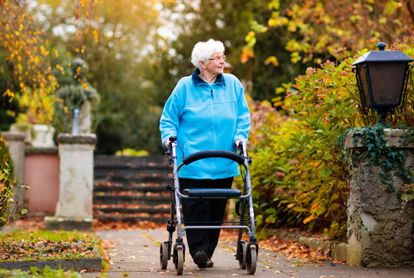 An elderly woman with a walker strolls down a scenic path.