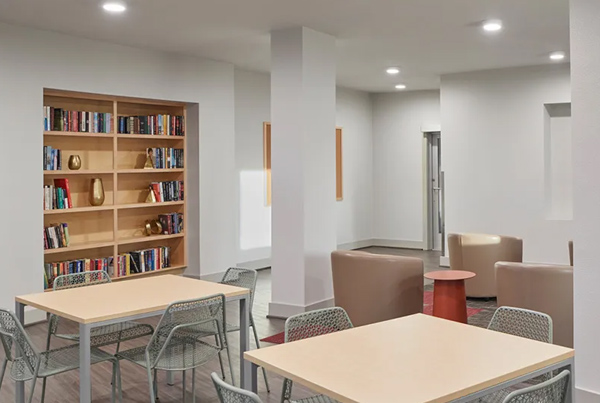 Community room with a table and chairs and large lounge chairs in the background.  