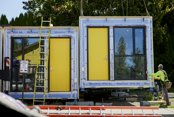 Two rectangular modules with a large window and yellow door, one of which is still attached to a crane.