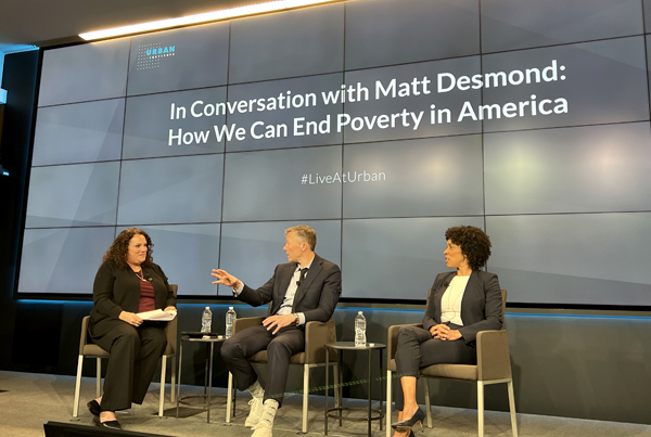 Mary Cunningham (left), Matthew Desmond (center), and Myra Jones-Taylor (right) sit and talk in front a screen that reads "In Conversation with Matt Desmond: How We Can End Poverty in America".