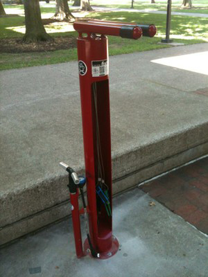 A Fix-it-Station, including a bike support, air pump, and repair tools, installed near a street curb on the University of Louisville campus.